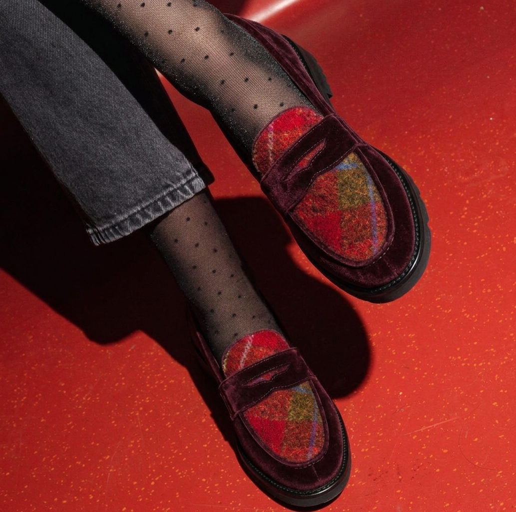 Burgundy velvet penny loafer with tartan insole on a red floor