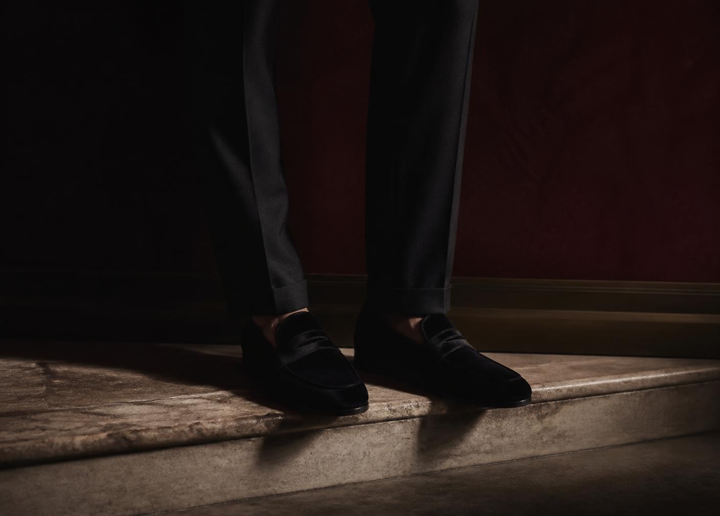 Men's black velvet penny loafers on a stone step